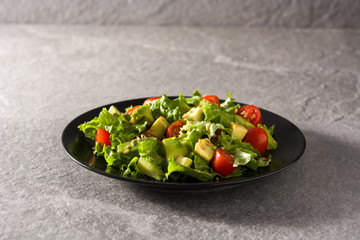 Salad with avocado, lettuce, tomato and flax seeds on gray background