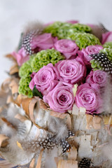 Beautiful spring bouquet close-up with pink roses and green carnations, decorated with feathers and birch bark. 