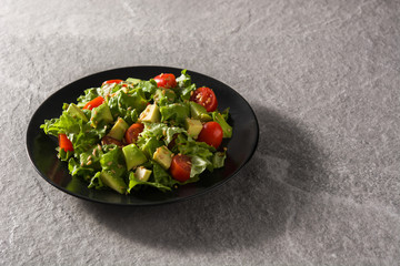 Salad with avocado, lettuce, tomato and flax seeds on gray background. Copy space