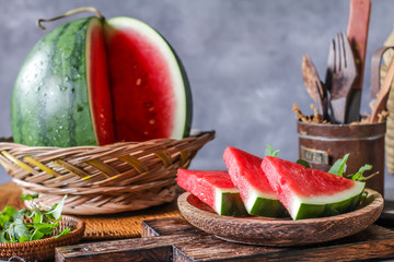 Photo of fresh watermelon with green leaves on wooden board over the table. Whole and sliced....