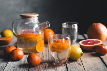 Citrus tea in a transparent teapot on a table with grapefruit and on a wooden table. Healthy drink.