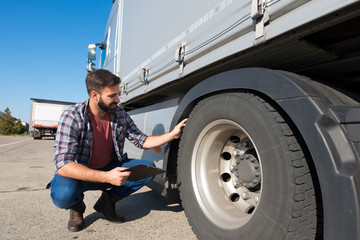 Truck driver inspecting tires and checking depth of tire tread for safe ride. Controlling vehicle before transportation service.