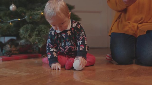 Adorable cute infant boy child playing with Christmas toy near decorated fir tree with granny. Family bonding. Winter holidays concept.