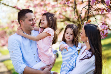 Young parents with small daugthers standing outside in spring nature.
