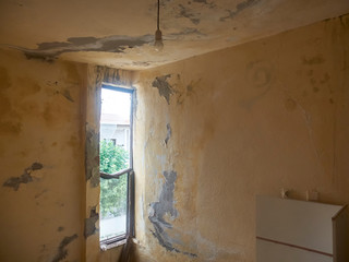 Interior of abandoned residential building with lightbulb hanging from the ceiling with peeling plaster