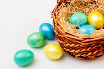 multicolored easter eggs in a brown basket of twigs on a white background
