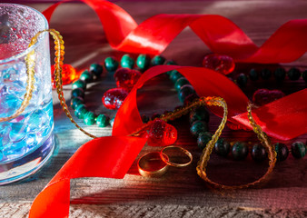 wedding still life malachite beads ice glass of water drops rings ribbons red on a wooden background low key