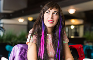 Fototapeta na wymiar Young stylish trendy woman with multi-coloured strand in hair sits in cafe