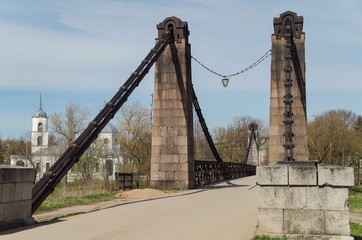 Chain bridge. Suspension bridge over the River Velikaya, opened in 1853. Trinity Cathedral (1780) away across the river. Russia, Pskov Oblast, Ostrov