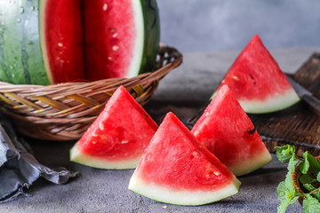 Photo of fresh watermelon with green leaves on wooden board over the table. Whole and sliced. Cutting board. Cut in halves. Dark background. Front view. Raw organic fruit. Image