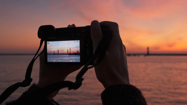Close-up of a woman's hands with a camera takes a photo of a bright sunset and the sea.
