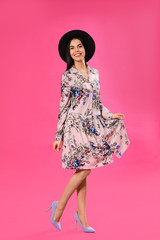Young woman wearing floral print dress and stylish hat on pink background