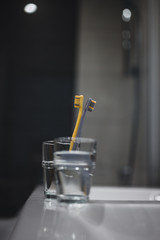 Two toothbrushes in glass cup in bathroom. Yellow and gray toothbrushes. Toothbrushes close up.