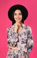 Young woman wearing floral print dress and stylish hat on pink background