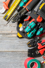 Tools electrician installer on a gray wooden table. Bag with construction tools for electrical installation