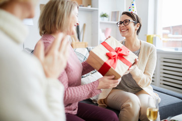 Portrait of three cheerful women celebrating birthday at home focus on young woman holding gift...
