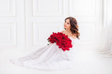 beautiful girl with a large bouquet of red roses in a white dress on a light background. Concept of holidays. Chic huge bouquet of flowers for Valentine's Day, Birthday and Mother's Day.