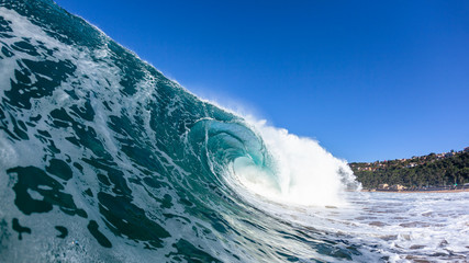 Hollow crashing ocean wave closeup swimming photo with textures on wall of water with blue sky panoramic beach coastline.