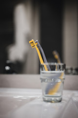 Two toothbrushes in glass cup in bathroom. Yellow and gray toothbrushes. Toothbrushes close up.