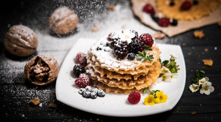 fresh viennese waffles with berries sprinkled with powdered sugar on blackboard on blank background