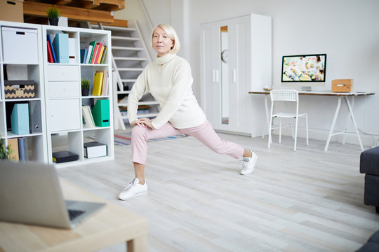 Full length portrait of active mature woman stretching legs during workout at home, copy space