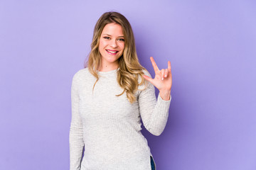 Young caucasian woman isolated on purple background showing a horns gesture as a revolution concept.