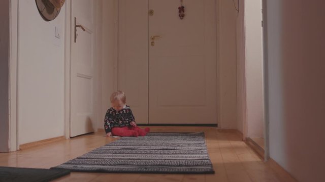 Adorable little toddler boy in Christmas sweater sitting on floor carpet playing looking around at home. Family concept.