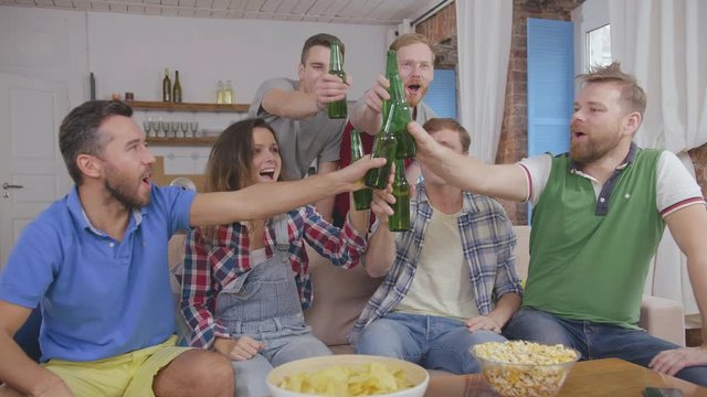 Happy sports fans clinking beer bottles and watching football game