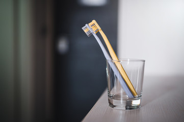 Two toothbrushes in glass cup in bathroom. Yellow and gray toothbrushes. Toothbrushes close up.