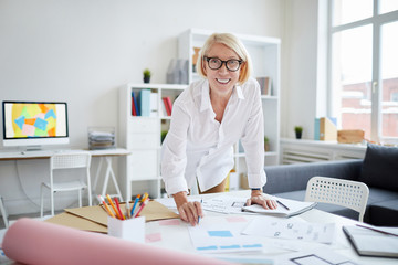 Portrait of smiling mature woman looking at camera while working with designs in modern office, copy space