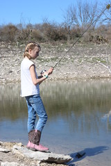 Blonde young girl with french braids and cowboy boots fishing in the lake