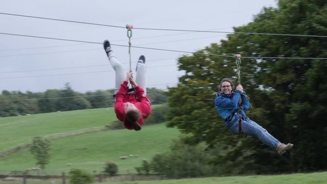 Two Girls hanging on Zip Wire / line - Aerial runway adventure in the outdoors. Slow Motion. 4K stock Video Clip Footage
