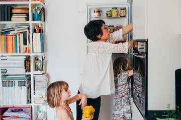 Two beautiful female toddler helping her mother unpacking groceries