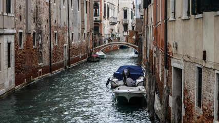 Venetian canal with a bridge between old historic houses and a boat moored to the wall.