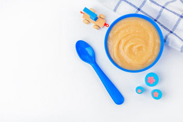 Baby food. Fresh homemade applesauce. Blue bowl with fruit puree on fabric and kids toys on table. The concept of proper nutrition and healthy eating. Organic and vegetarian food. Copy space for text
