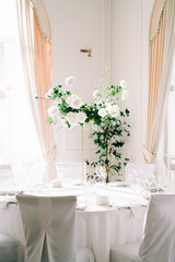 Fototapeta na wymiar floral decoration of wedding tables, delicate white flowers and branches of fresh greenery on white hall