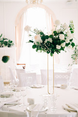floral decoration of wedding tables, delicate white flowers and branches of fresh greenery on white hall