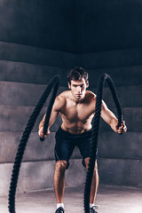 Muscular powerful man training with rope.