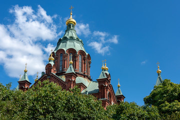 Fototapeta na wymiar Republic of Finland, Helsinki: Dome of famous Uspenski Cathedral with green trees and blue sky in the city center of the Finnish capital - concept Christianity orthodox church religion sightseeing