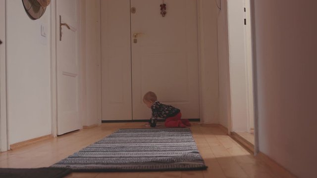 Cute lovely little boy baby in sweater crawling on the floor carpet in corridor playing in the house. At home. Concept of childhood.
