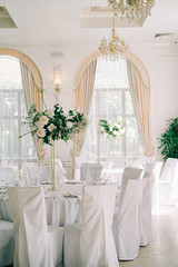 floral decoration of wedding tables, delicate white flowers and branches of fresh greenery on white hall