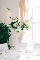 Fototapeta na wymiar beautiful floral arrangement of delicate rose flowers and fresh greenery in the design of the wedding table in the white hall