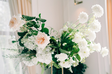 beautiful floral arrangement of delicate rose flowers and fresh greenery in the design of the wedding table in the white hall