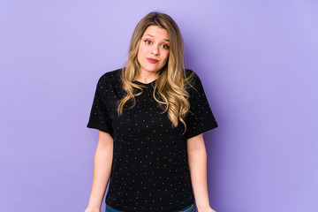 Young caucasian woman isolated on purple background shrugs shoulders and open eyes confused.