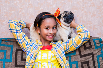 Cute little indian girl playing with her pet dog pug inside home