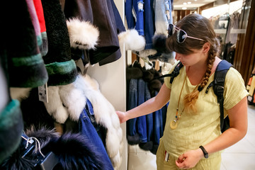 natural fur coats weigh on hangers in a store. .girl in a yellow sweater chooses a fur coat in a store