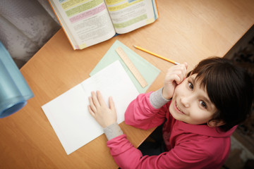Naklejka premium Smiling little asian schoolgirl doing homework.