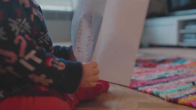 Excited adorable toddler baby boy wearing xmas sweater holding a colorful interesting picture playing on the floor at home. Concept of childhood.