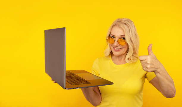 Portrait of happy exited abult lady with laptop isolated over the yellow studio