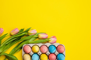 Fototapeta na wymiar Bouquet of tulips and colorful eggs on yellow Easter background, empty copyspace